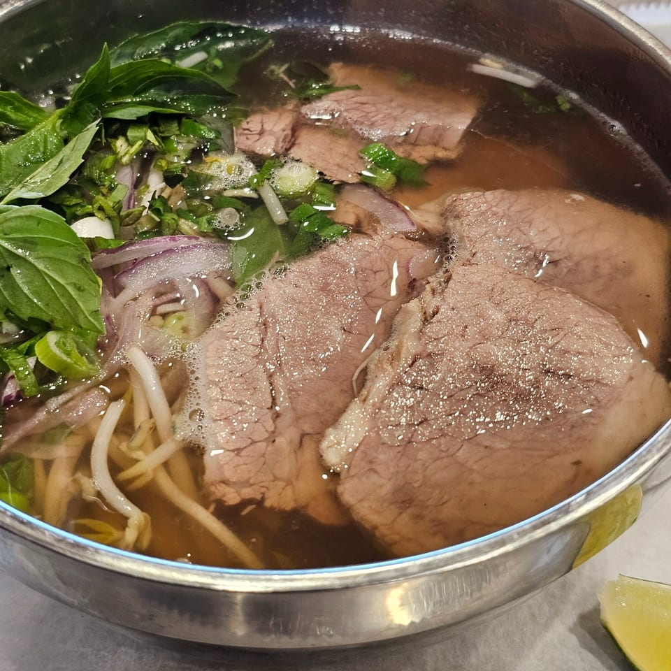 Close-up of a bowl of Vietnamese pho with beef, noodles, herbs, and broth.