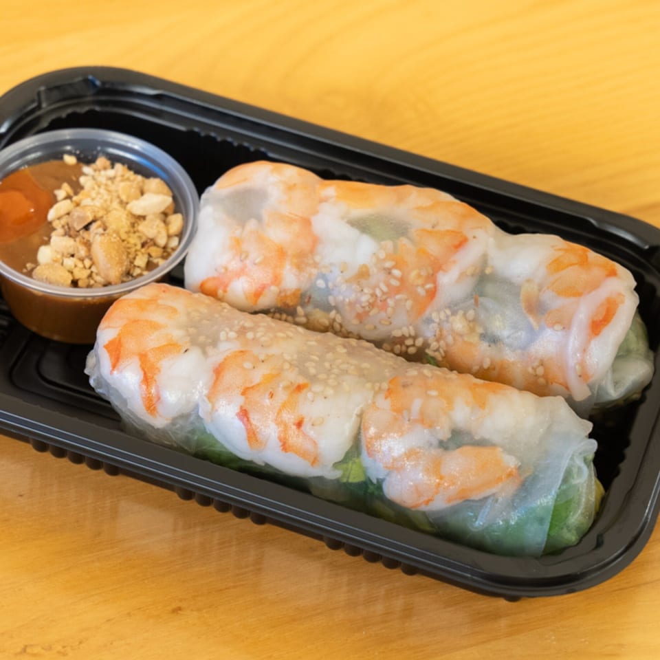 Two Vietnamese shrimp spring rolls with sesame seeds and a side of peanut sauce with crushed peanuts.