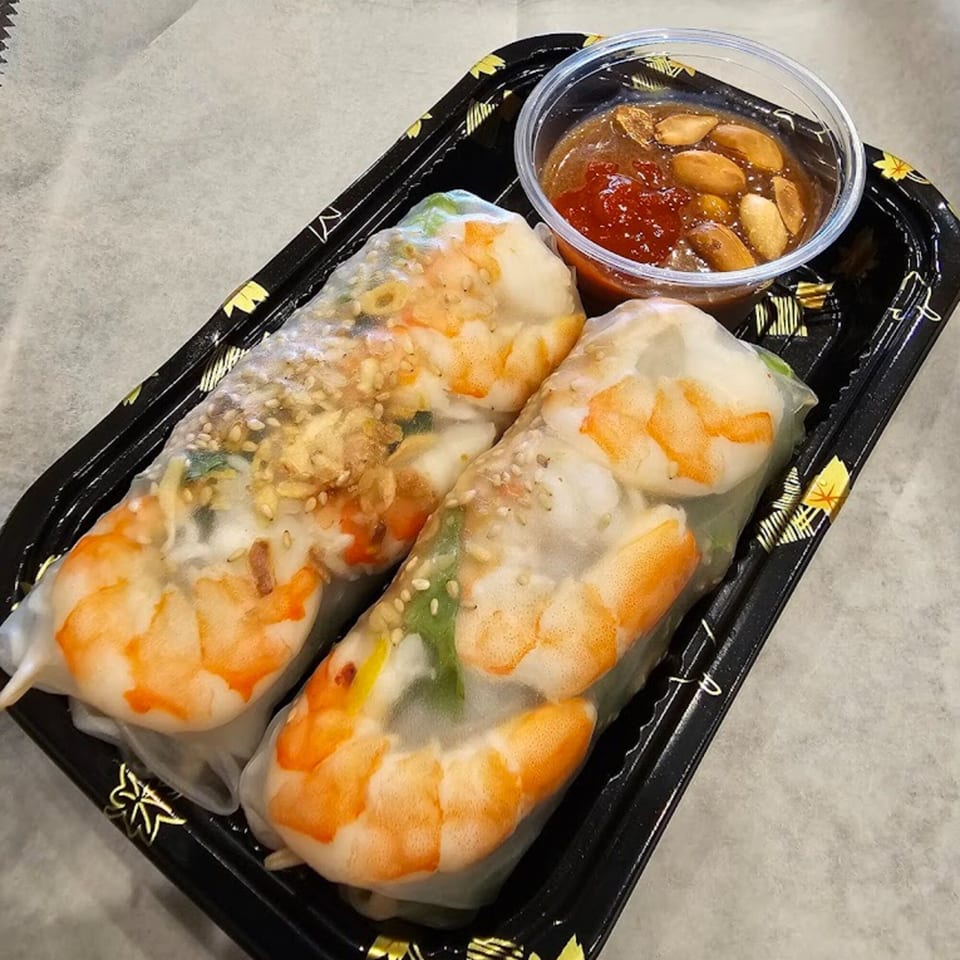 Two fresh Vietnamese spring rolls with shrimp and a side of peanut dipping sauce.