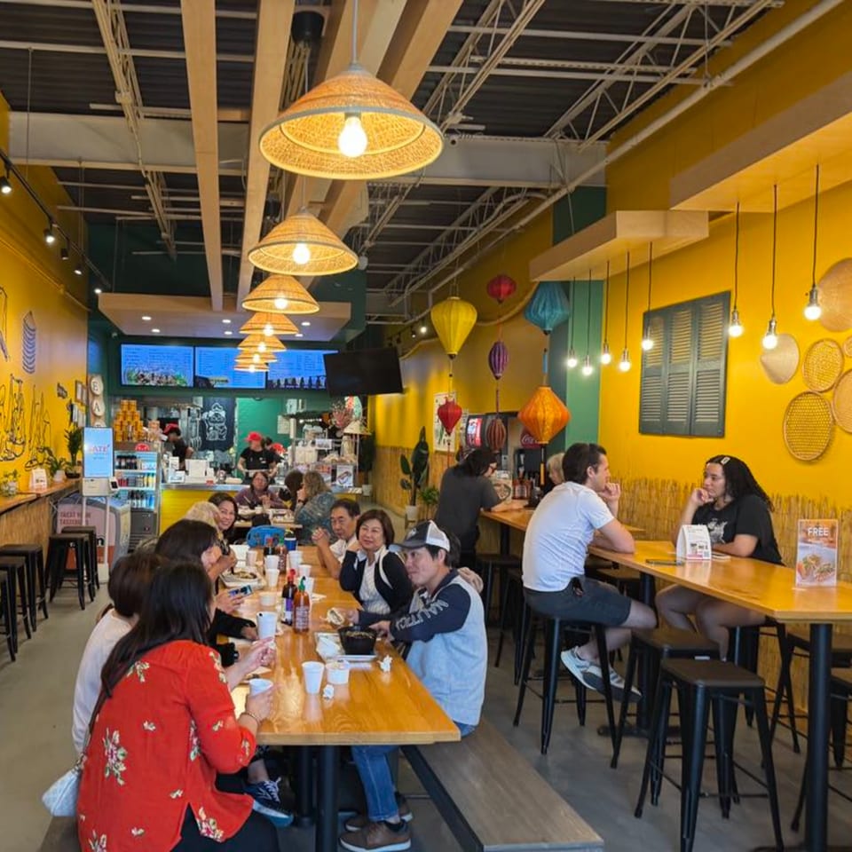 Diners enjoying Vietnamese food at SATE Banh Mi & Grille, with vibrant yellow walls and bamboo decor.