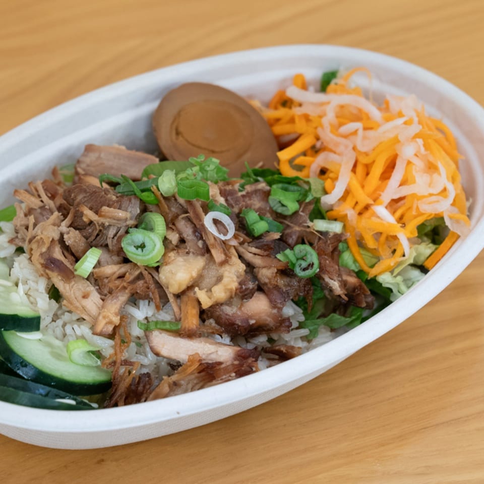 Vietnamese rice bowl with shredded pork, sliced cucumbers, pickled carrots, and a brown egg.
