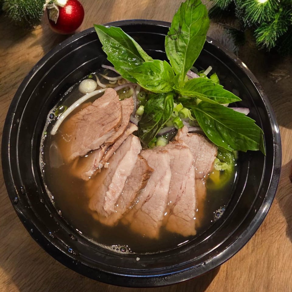 Vietnamese pho with sliced beef, noodles, and fresh basil in a black bowl, with Christmas decor.
