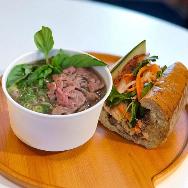A SATE Banh Mi & Grille pho bowl with beef and herbs next to a banh mi sandwich.