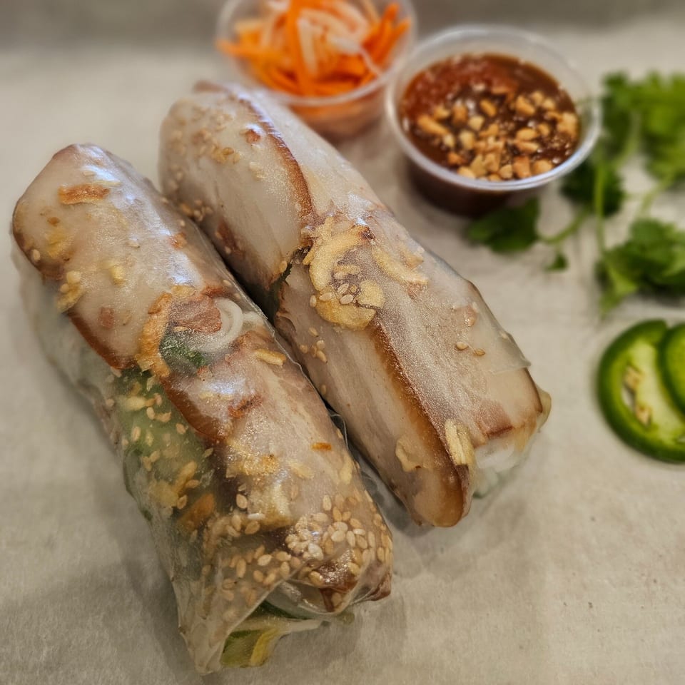 Two Vietnamese spring rolls with pork and sesame seeds, served with peanut sauce and pickled vegetables.