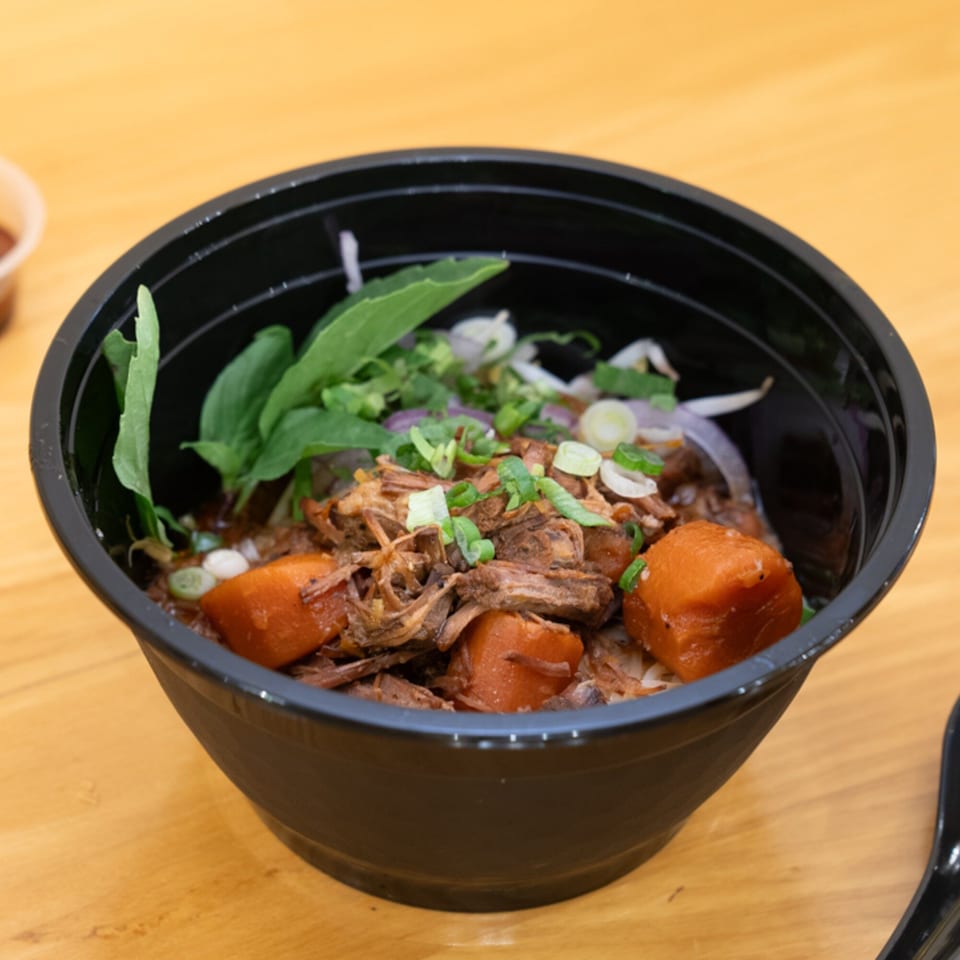 Vietnamese beef stew with carrots, onions, and herbs in a black bowl on a wooden table.