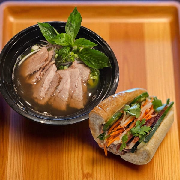 A bowl of Vietnamese pho with beef and basil, next to a banh mi sandwich on a wooden tray.