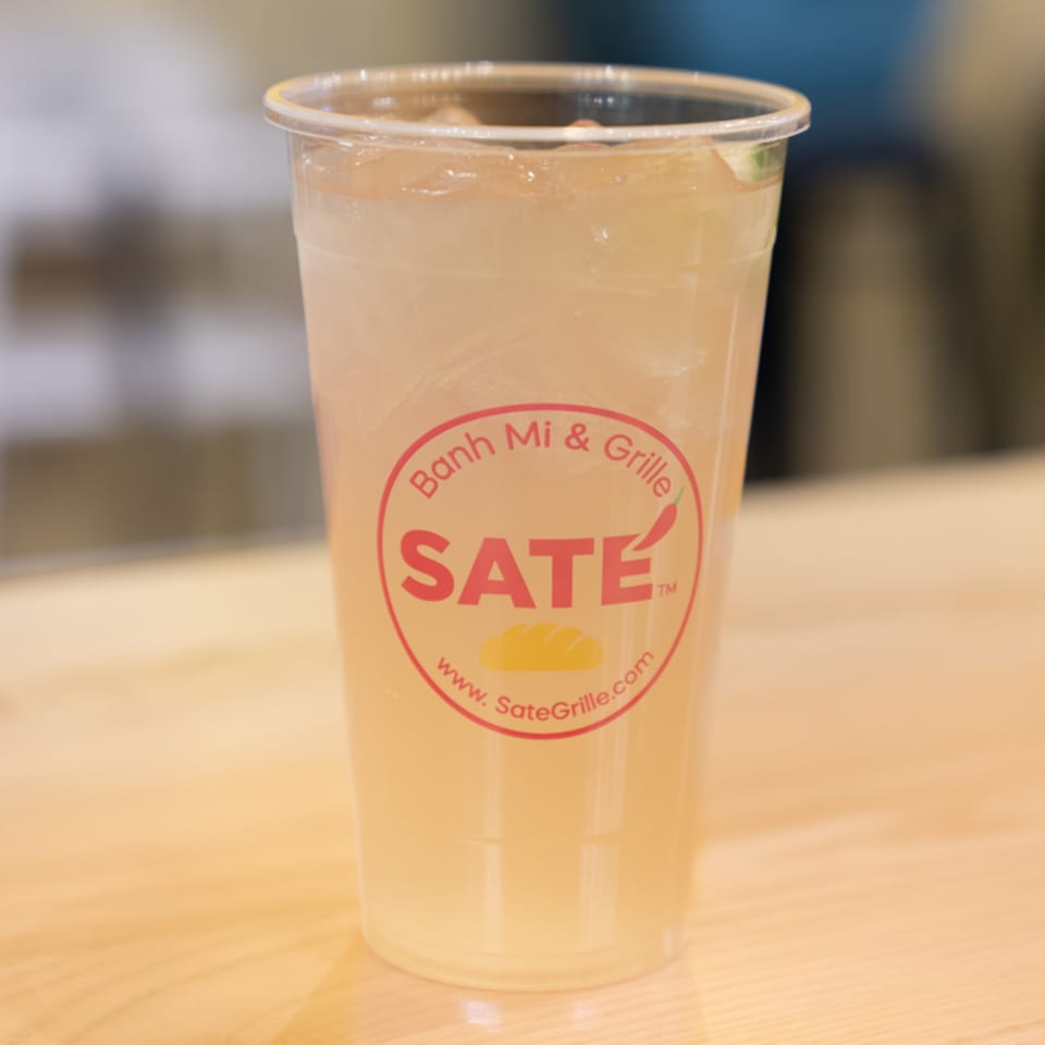 Iced beverage in a clear plastic cup with the SATE Banh Mi & Grille logo.