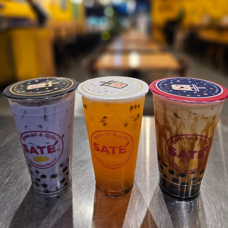 Three SATE Banh Mi & Grille bubble tea drinks, taro, passion fruit, and brown sugar, on a metal surface.