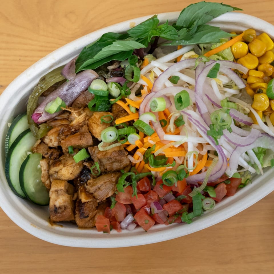 Vietnamese grilled chicken bowl with cucumbers, corn, tomatoes, onions, and fresh herbs.