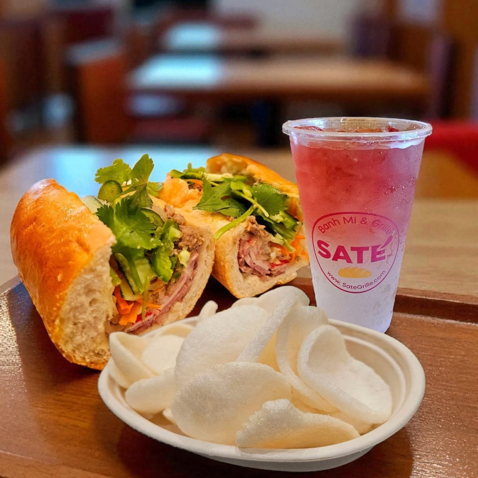 SATE Banh Mi & Grille's banh mi sandwich, shrimp chips, and a red drink on a wooden tray.