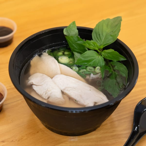 A black bowl of SATE Banh Mi & Grille's chicken pho with basil and green onions.
