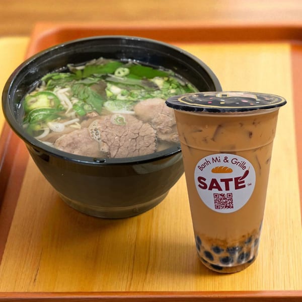 A bowl of SATE Banh Mi & Grille pho with beef, vegetables, and a boba tea.
