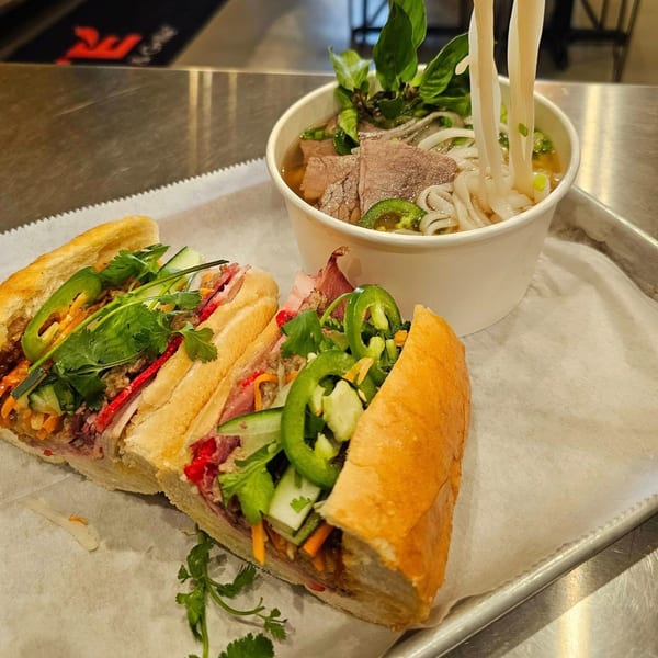 Two SATE Banh Mi sandwiches and a bowl of pho with noodles being lifted.
