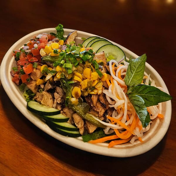 Vietnamese bowl with grilled meat, corn, tomatoes, cucumbers, pickled daikon, carrots, and basil.