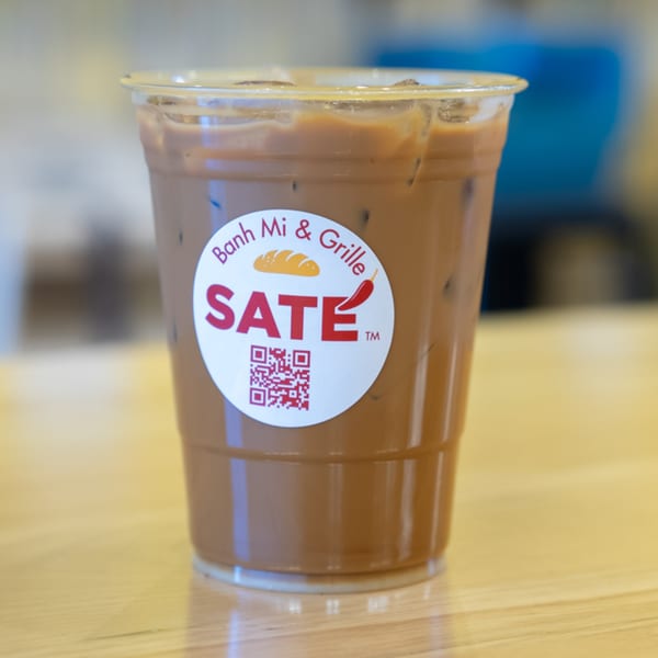 Iced Vietnamese coffee in a clear plastic cup with the SATE Banh Mi & Grille logo.