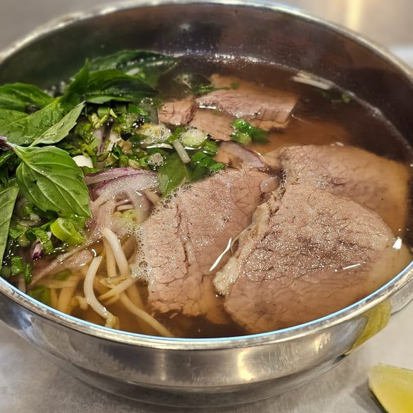 Close-up of a bowl of Vietnamese pho with beef, noodles, basil, and bean sprouts.