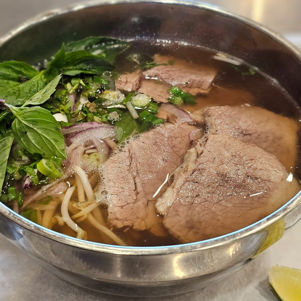 Close-up of a bowl of Vietnamese pho with beef, noodles, basil, and bean sprouts.
