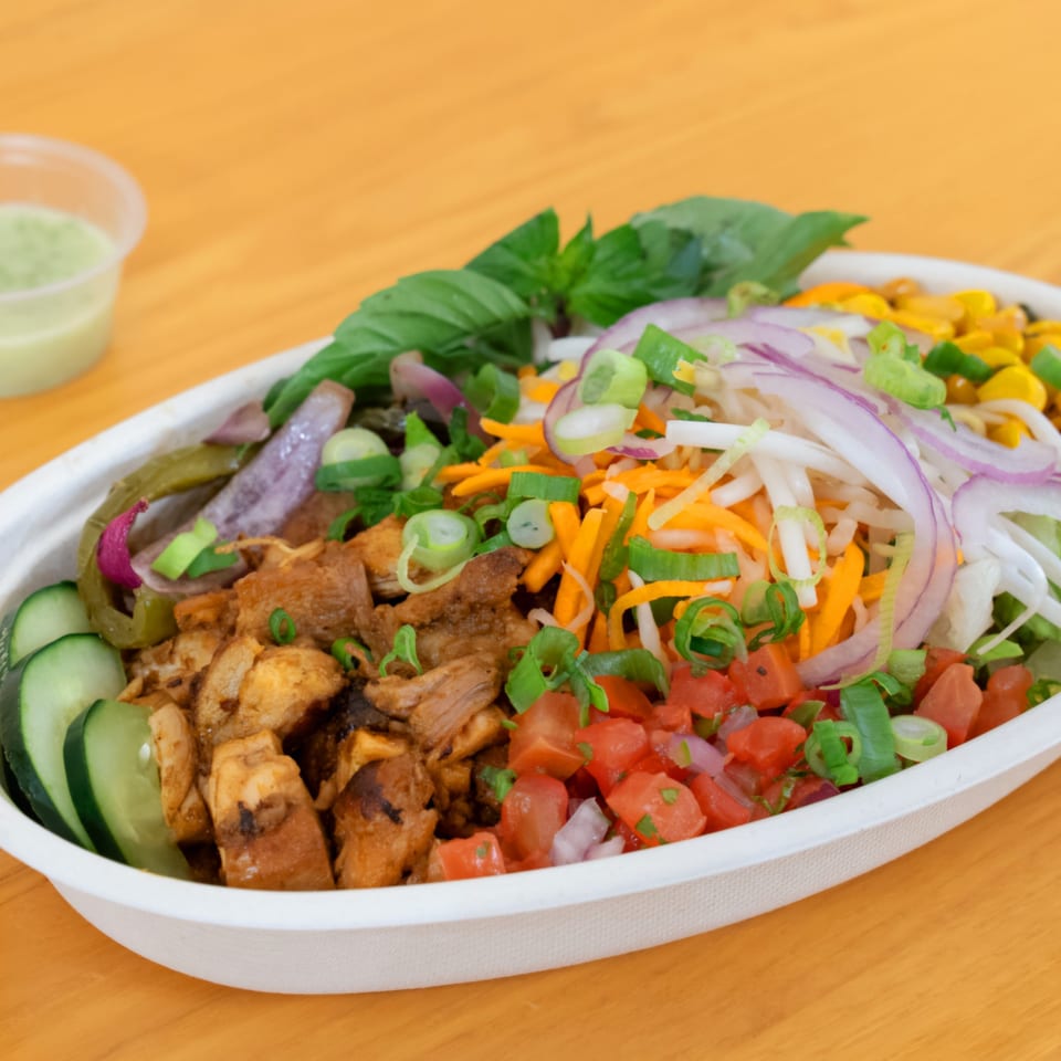 A SATE Banh Mi & Grille bowl with chicken, cucumbers, peppers, onions, carrots, and tomatoes.