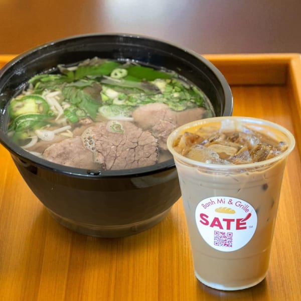 A bowl of SATE Banh Mi & Grille pho with beef and herbs, next to an iced coffee.