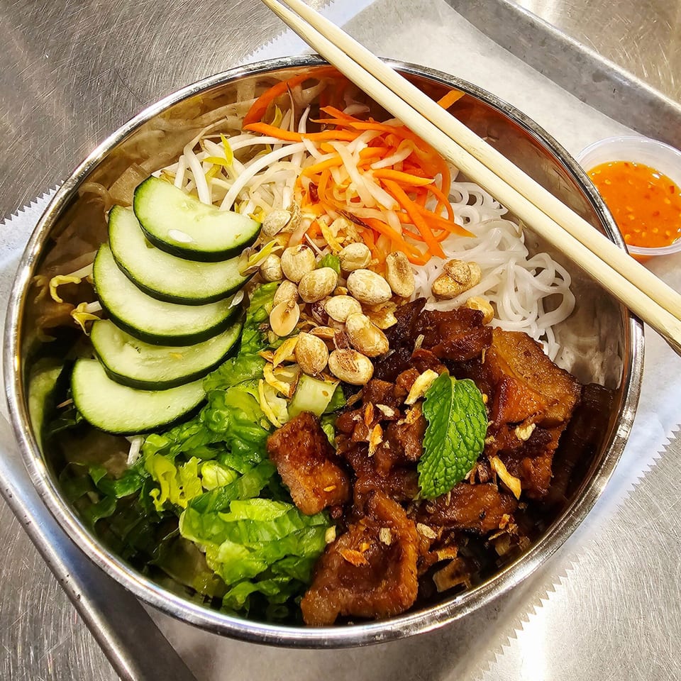 Vietnamese vermicelli bowl with grilled pork, fresh vegetables, peanuts, and chopsticks in a metal bowl.