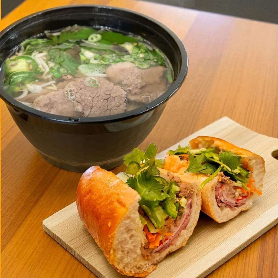 A bowl of SATE Banh Mi & Grille pho with beef and herbs next to a banh mi sandwich.