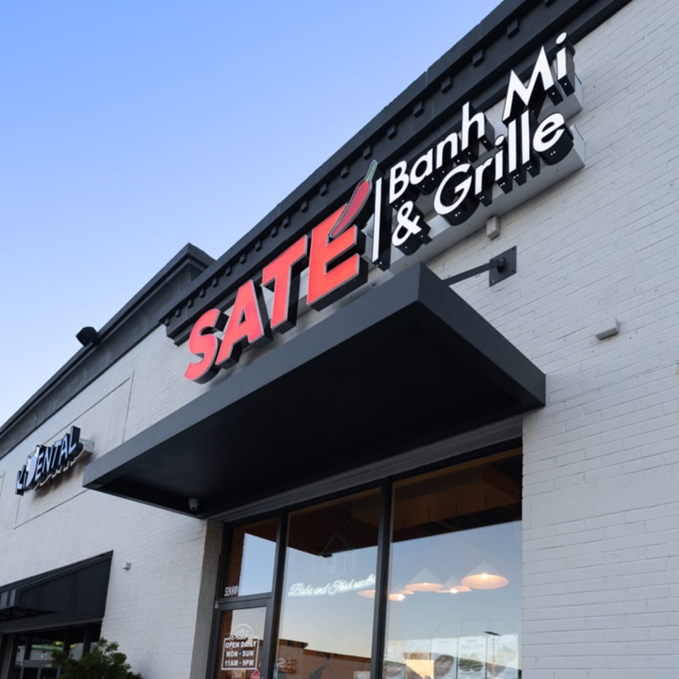 Exterior view of SATE Banh Mi & Grille, featuring its red and white sign on a white brick building.
