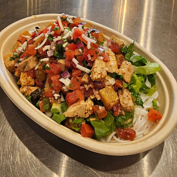 Vietnamese bowl with chicken, rice noodles, lettuce, tomatoes, onions, and shredded cheese.