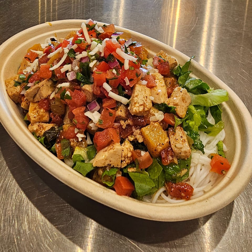 Vietnamese bowl with chicken, rice noodles, lettuce, tomatoes, onions, and shredded cheese.