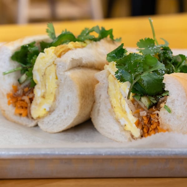 Two SATE Banh Mi & Grille sandwiches with egg, cilantro, and pickled carrots on a tray.