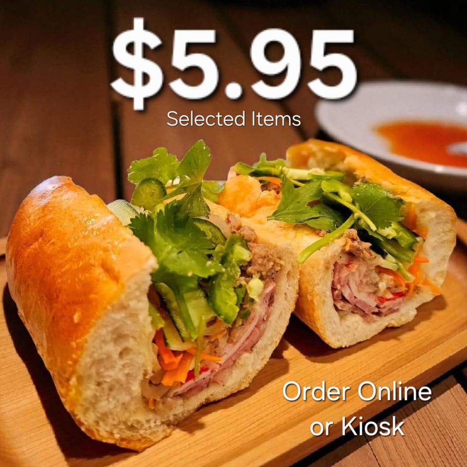 Two Vietnamese banh mi sandwiches, filled with meat and fresh vegetables, on a wooden board.