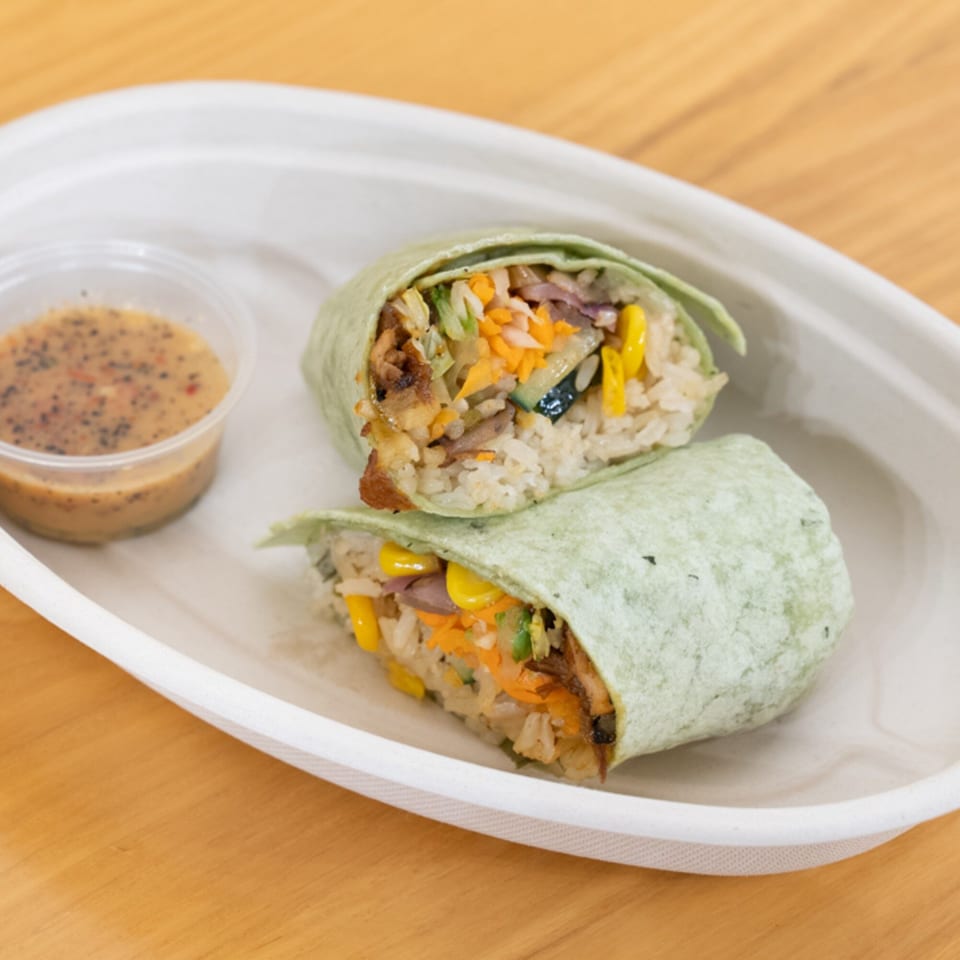 Two halves of a Vietnamese burrito, filled with rice, meat, and vegetables, with a side of sauce.
