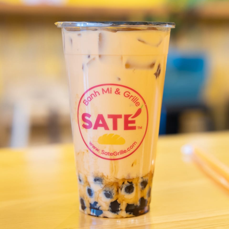 SATE Banh Mi & Grille bubble tea with tapioca pearls and the restaurant logo on a wooden table.