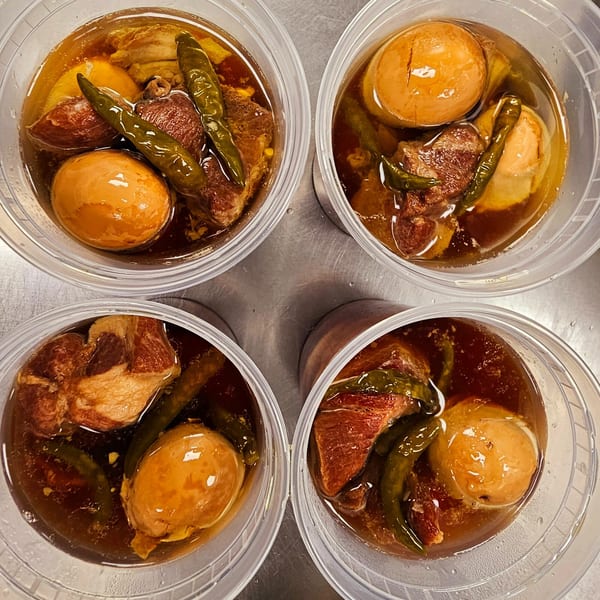 Four clear containers of Vietnamese Thit Kho, braised pork and eggs, with green chilies.