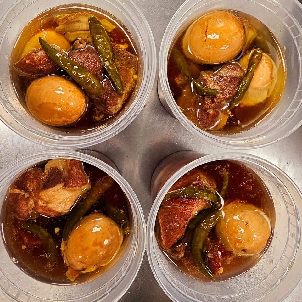 Four clear containers of Vietnamese Thit Kho, braised pork and eggs, with green chilies.