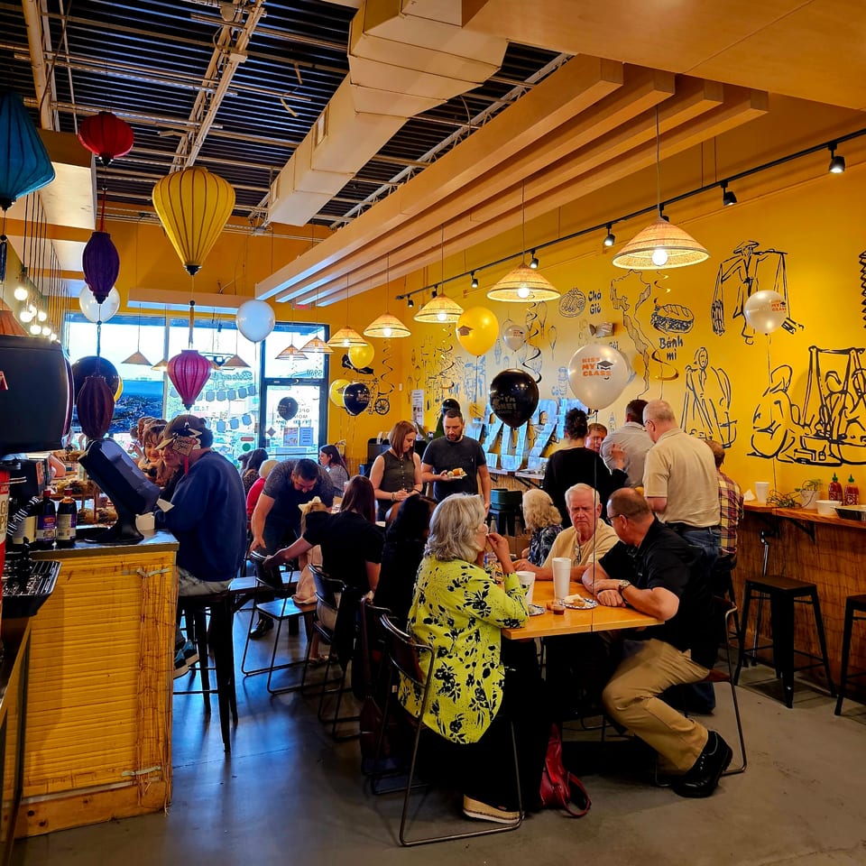 A bustling SATE Banh Mi & Grille dining room with patrons eating and colorful lanterns hanging.