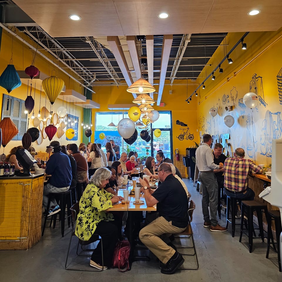 Diners enjoying Vietnamese food in a vibrant, yellow-walled SATE Banh Mi & Grille restaurant.